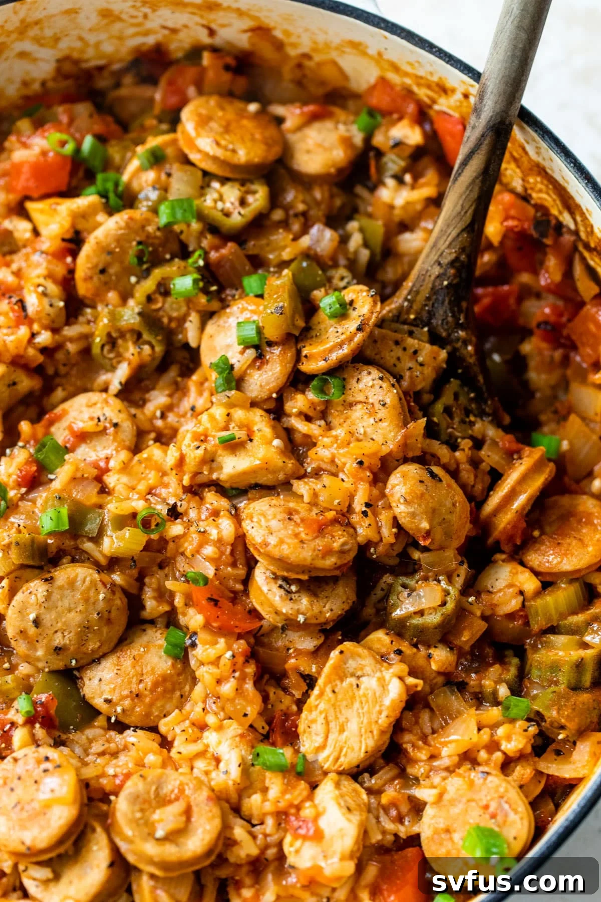 Close-up of chicken and sausage jambalaya in a Dutch oven with a wooden spoon, showcasing rich texture and vibrant colors.