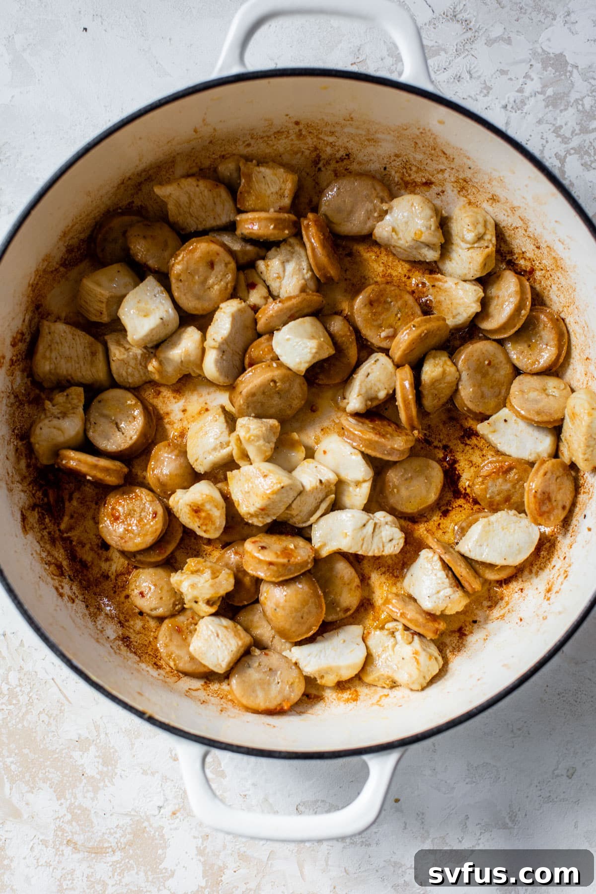 Chicken and sausage pieces browning in a Dutch oven, ready to be removed.