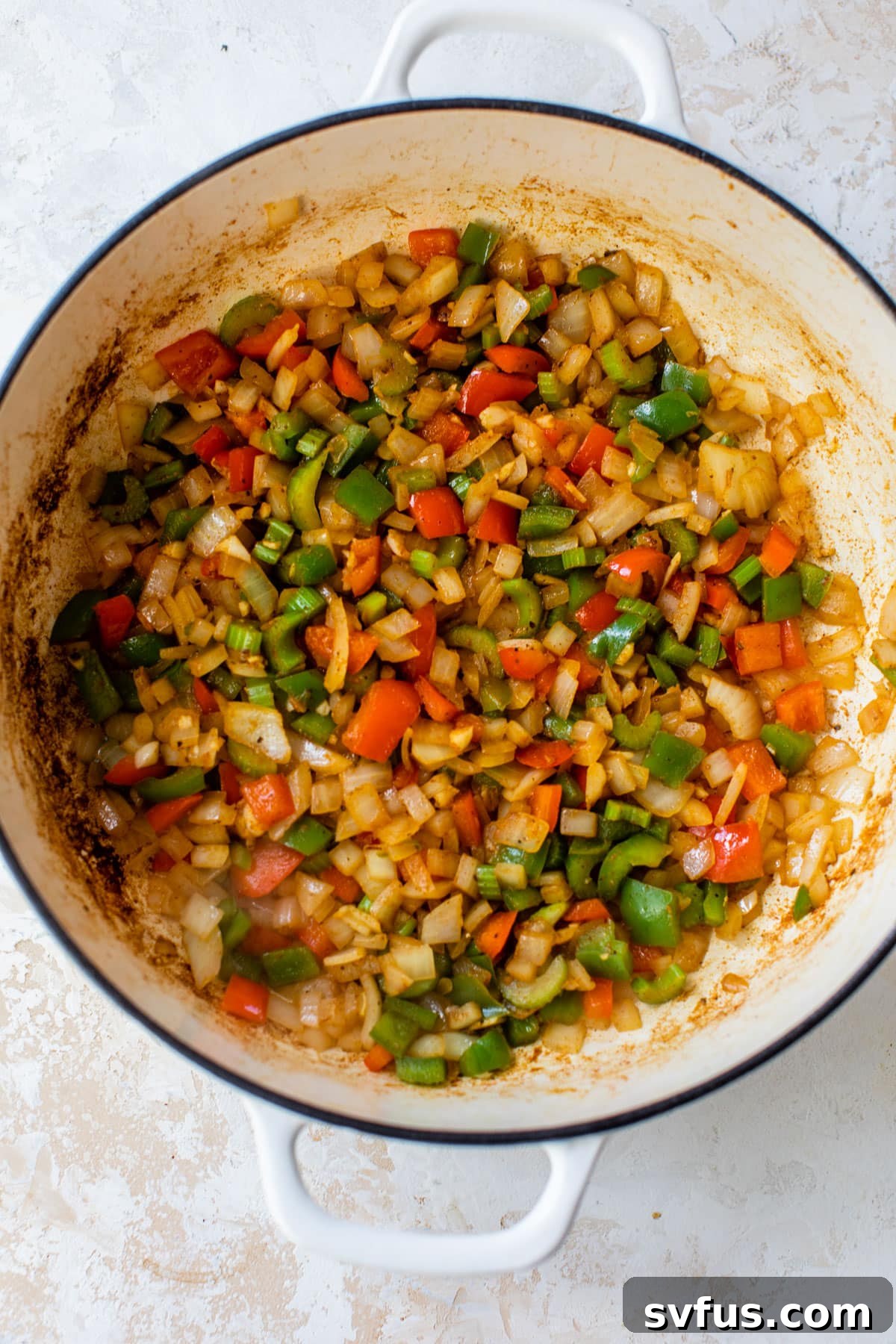 Diced bell peppers, onion, and celery cooking in a Dutch oven, forming the aromatic base of the jambalaya.