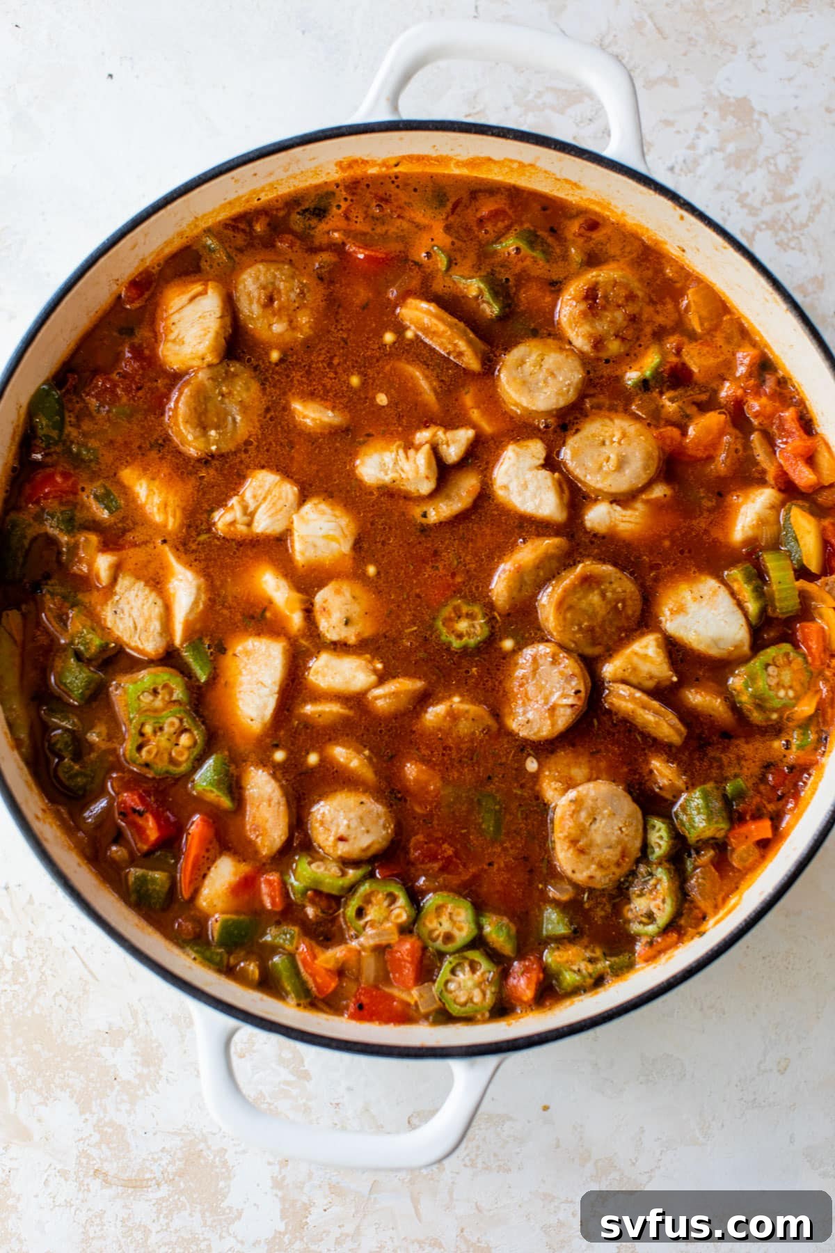 Chicken and sausage mixed into the Dutch oven with rice, vegetables, and broth, ready for simmering.