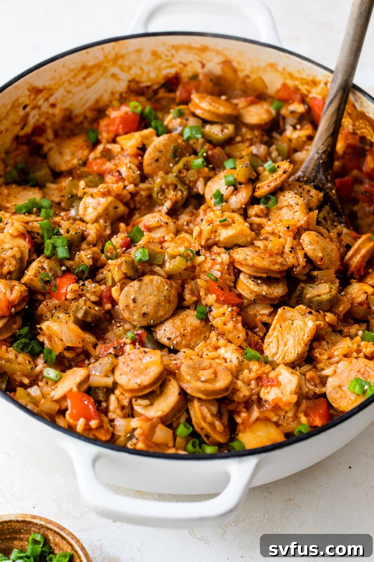 Finished chicken and sausage jambalaya in a Dutch oven with a wooden spoon, garnished and ready to serve.