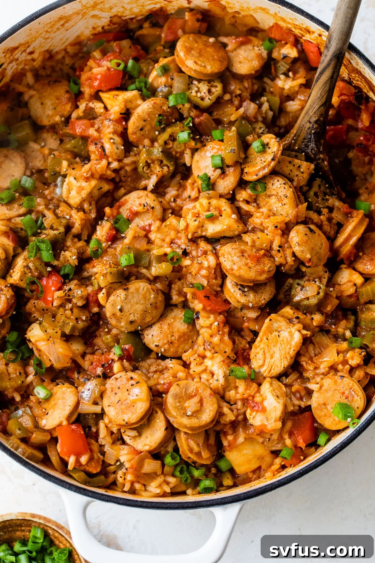 Overview shot of chicken and sausage jambalaya in a Dutch oven with a wooden spoon, garnished and ready to serve.