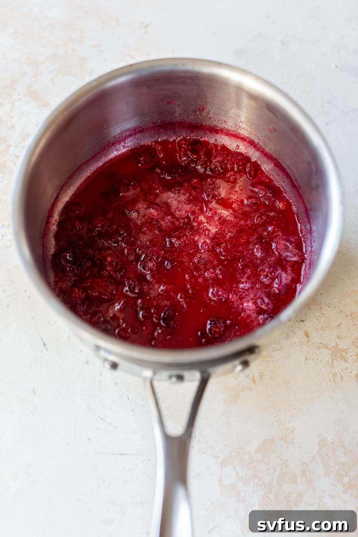 Overhead view of simmered cranberry syrup in a saucepan, cranberries broken down.