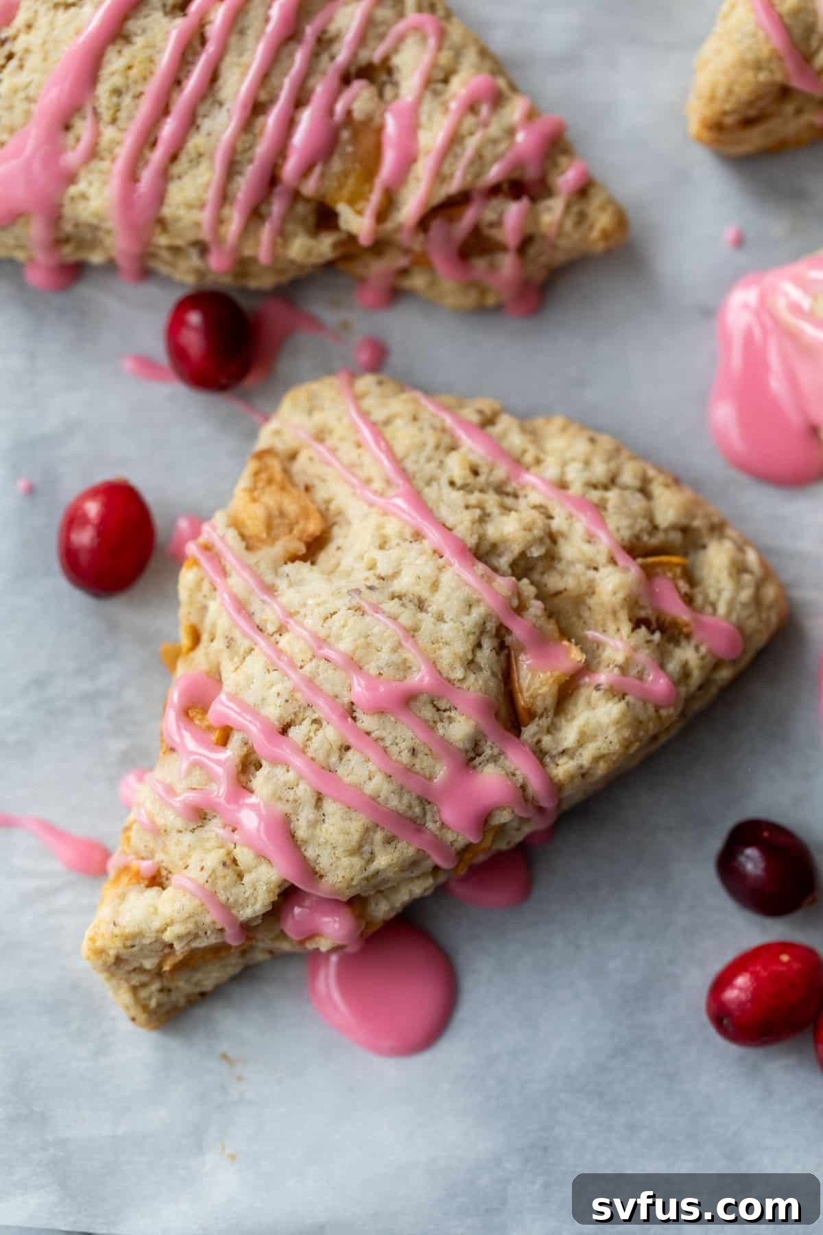Overhead view of two vegan Apple Cranberry Scones drizzled with pink cranberry glaze, with fresh cranberries on the side.