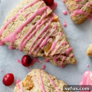 Overhead view of 3 apple cranberry scones topped with a drizzle of pink cranberry glaze with fresh cranberries on the side.