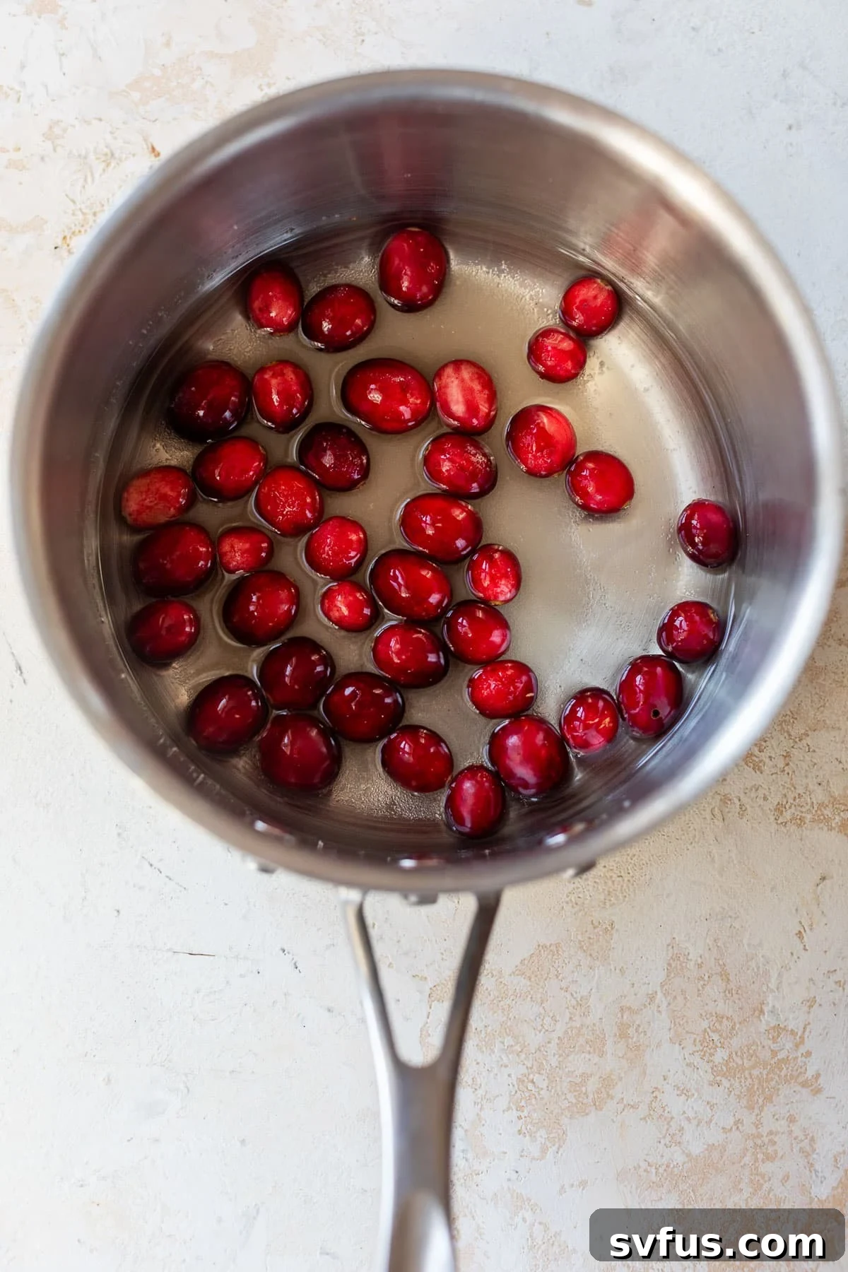 Overhead view of cranberries, water, and sugar simmering in a saucepan for cranberry syrup.