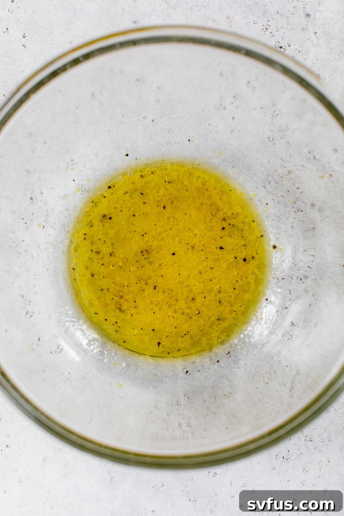 Ingredients for the lemon dressing in a glass bowl, ready to be whisked together.