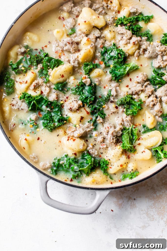 Close-up of a skillet filled with a finished one-pot gnocchi dish, featuring sausage and wilted kale.