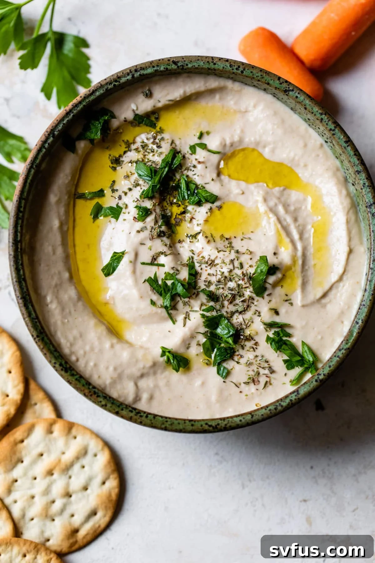 A bowl of white bean hummus, perfectly smooth and garnished, ready to be served or stored.