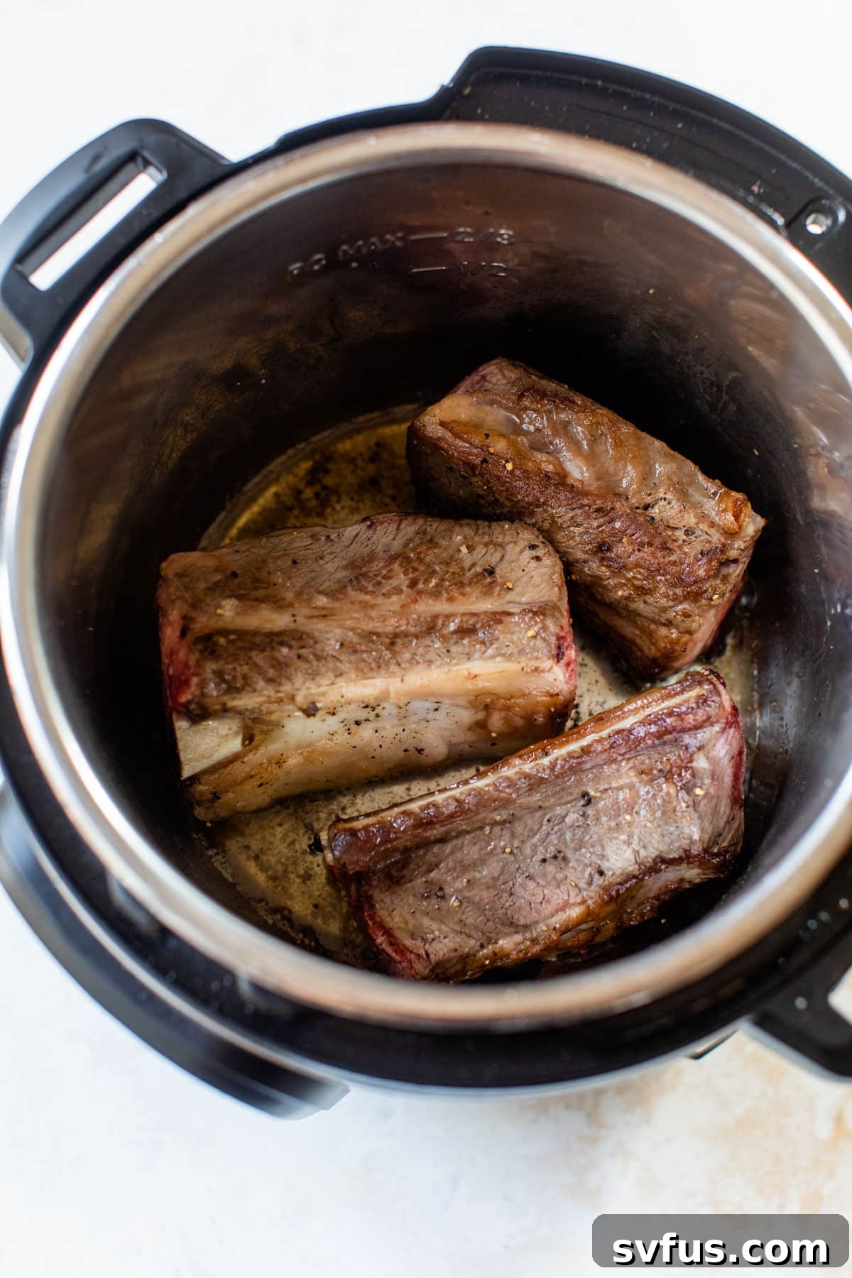 Raw short ribs being placed into an Instant Pot to sear.