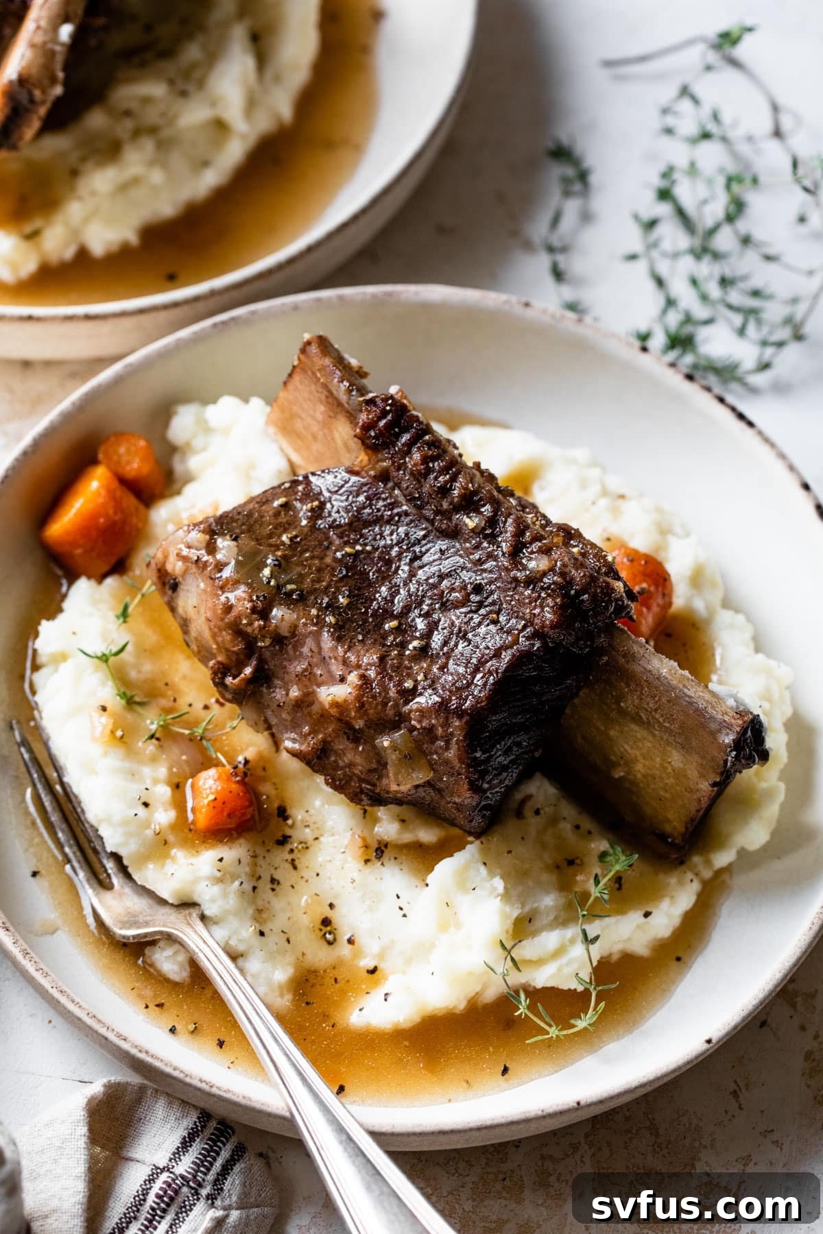 A close-up view of perfectly cooked Instant Pot Short Ribs, resting on creamy mashed potatoes, generously covered in a glossy red wine gravy, with a fork ready to enjoy.