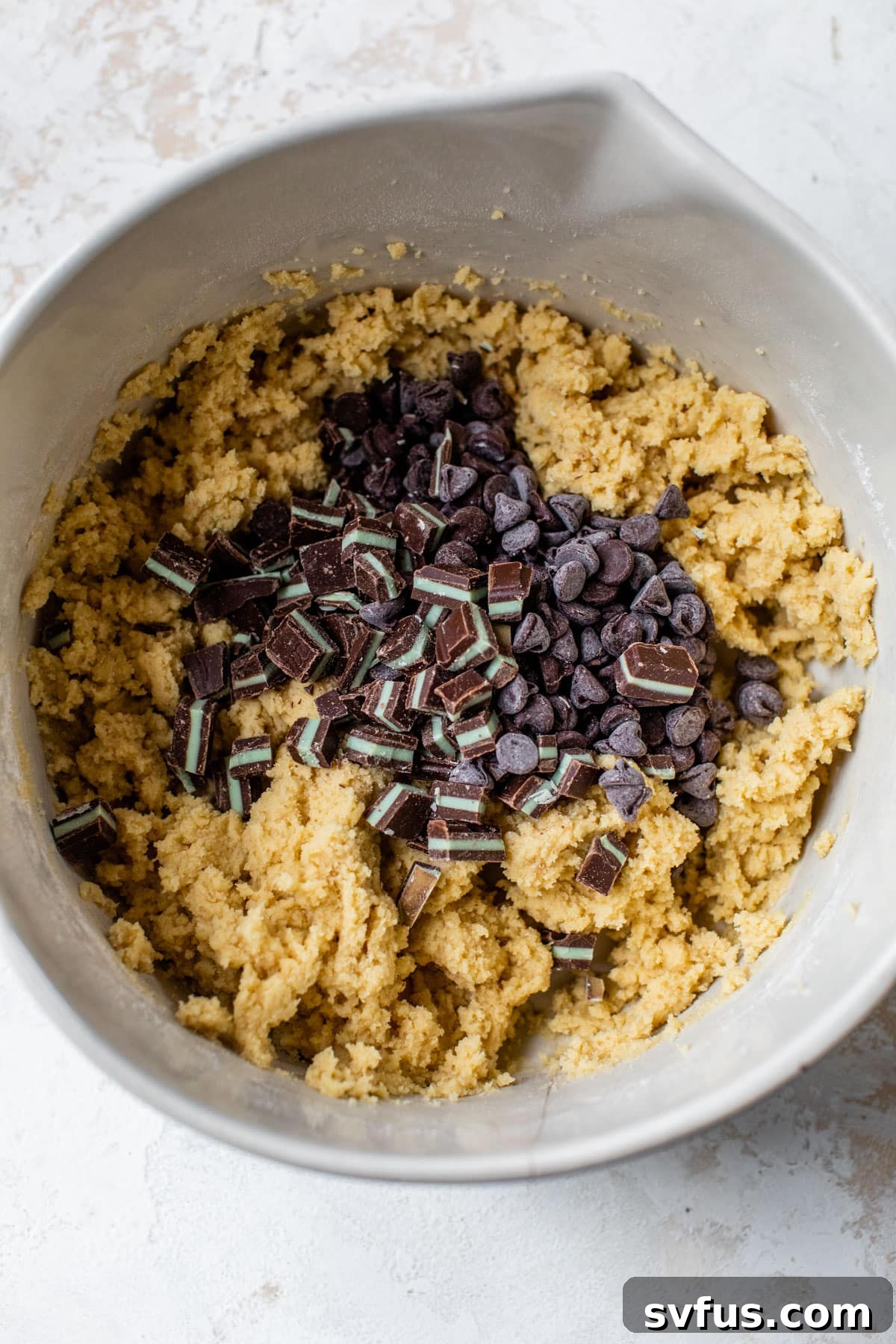 Cookie dough in a large bowl with chocolate chips and chocolate mint pieces folded in