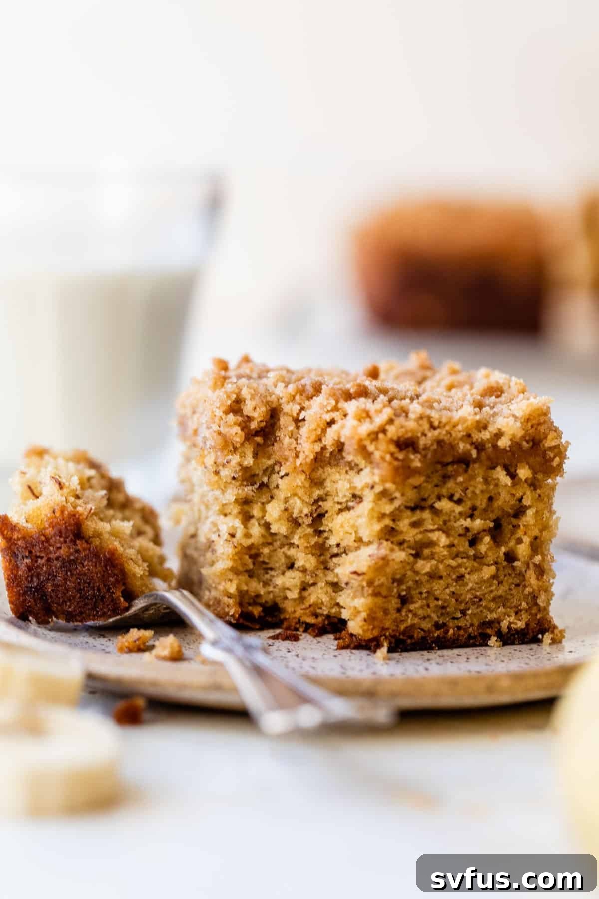 side view of a slice of banana coffee cake with a bite taken out on a plate with a fork