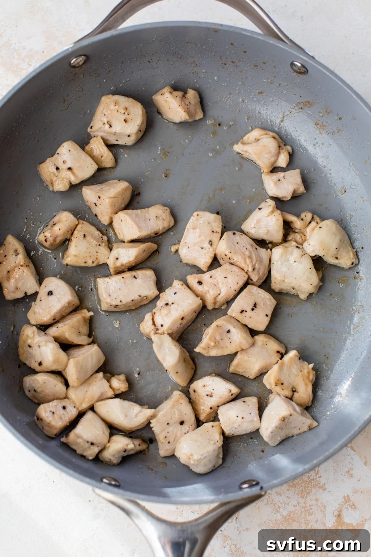 Diced chicken pieces searing in a hot skillet with olive oil, acquiring a golden brown crust.