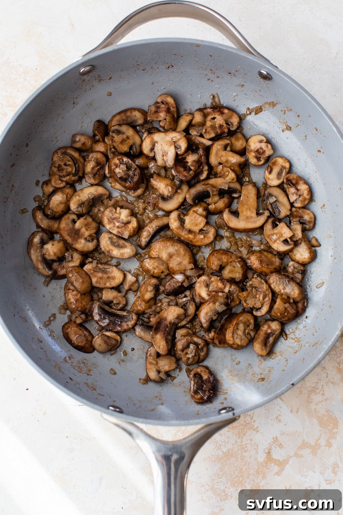 Sliced mushrooms and minced shallots sautéing in a skillet with butter, becoming tender and fragrant.