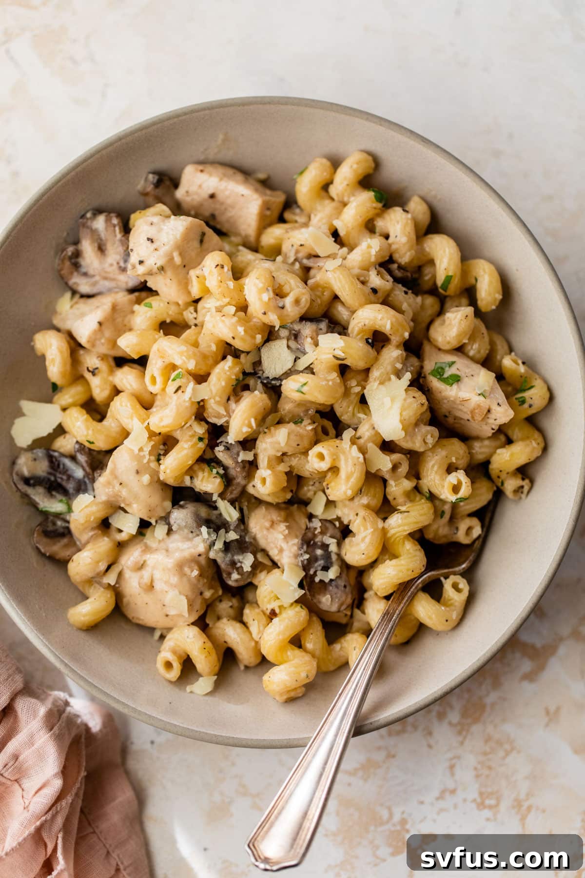 A bowl of creamy chicken mushroom pasta, garnished with fresh parmesan cheese and a a fork taking a bite.