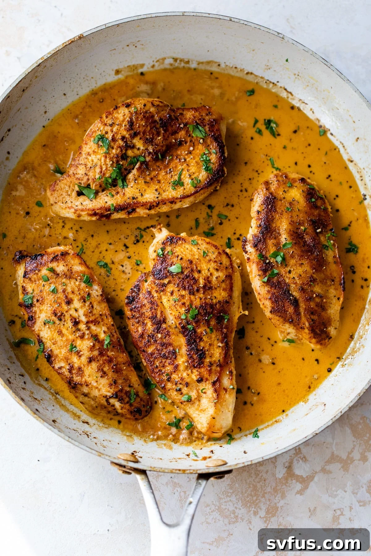 Four pieces of cooked Cajun chicken resting in a large skillet, generously topped with freshly chopped parsley.