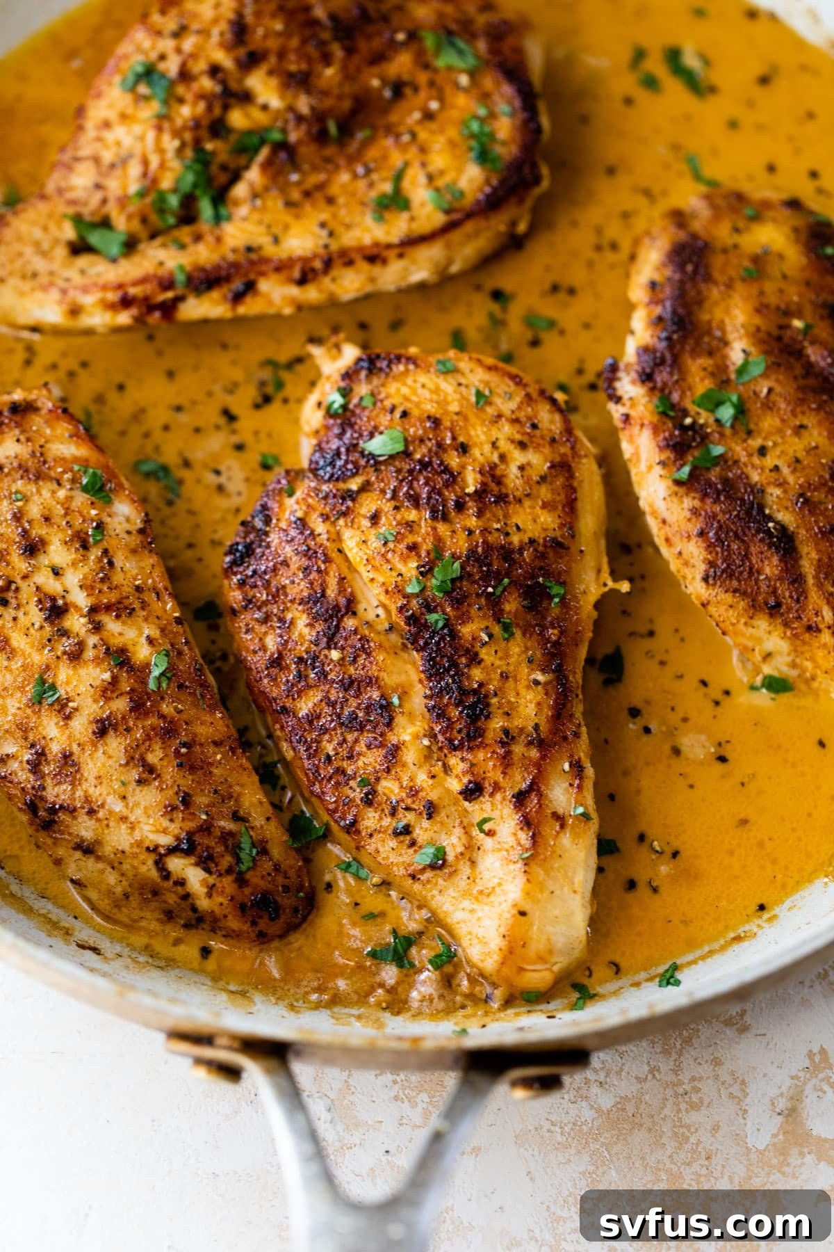 A close-up view of a skillet filled with creamy Cajun chicken, adorned with fresh chopped parsley, ready to be served.