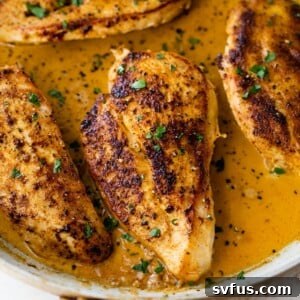 Close-up of creamy Cajun chicken in a large skillet with fresh chopped parsley.