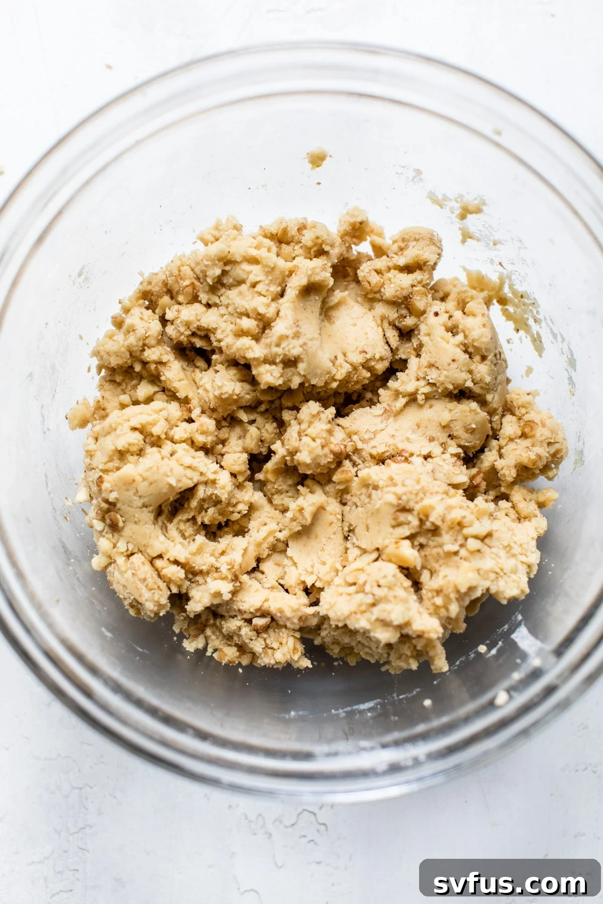 Cookie dough mixture in a clear glass mixing bowl, appearing soft and ready for forming