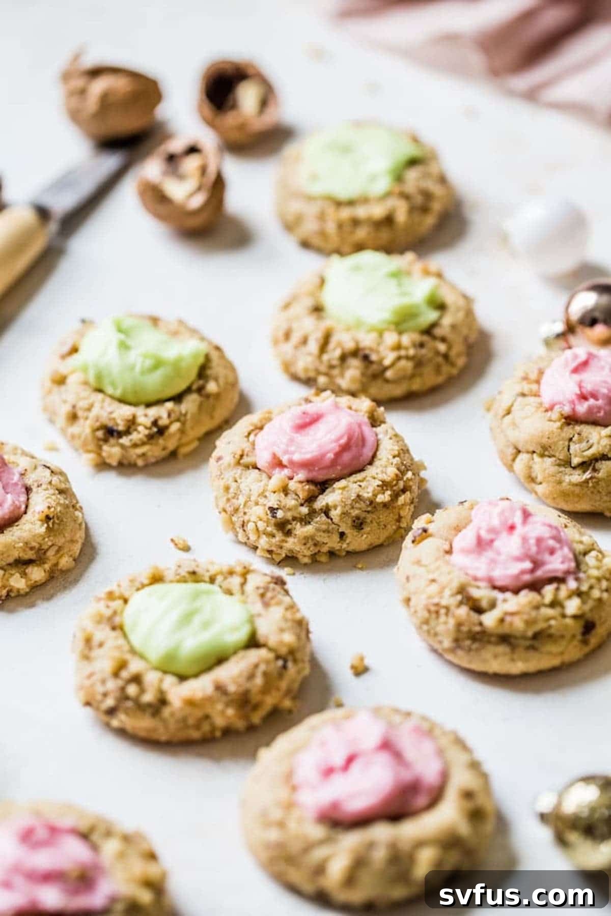 Beautifully arranged thumbprint cookies with vibrant red and green icing and walnut toppings on a rustic wooden table, ready to be enjoyed by friends and family