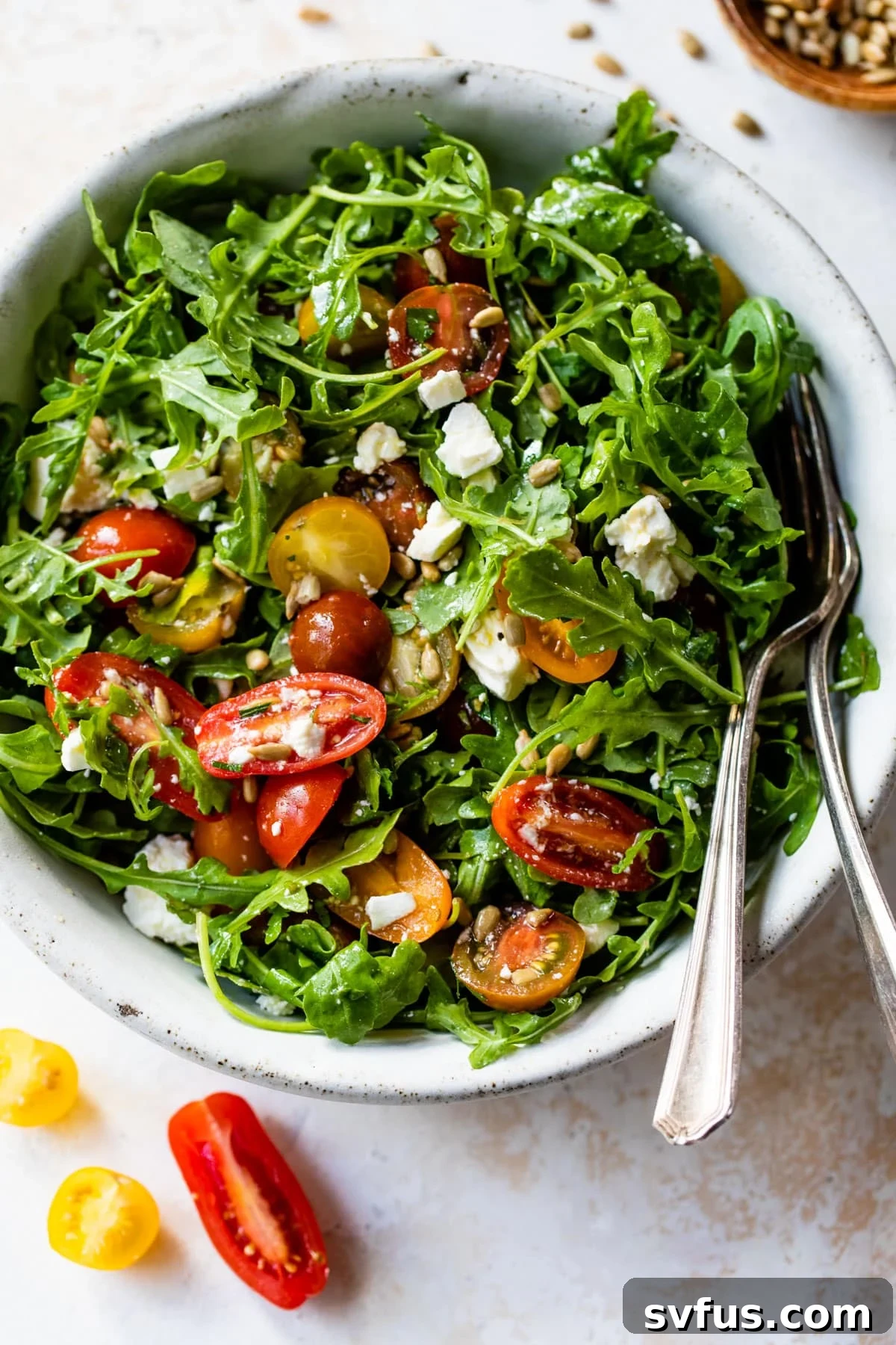 Close-up of a fresh arugula salad in a bowl with a fork, generously topped with vibrant sliced grape tomatoes, ready to be enjoyed.