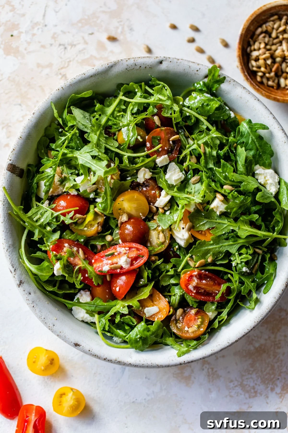 A vibrant arugula salad in a large serving bowl, beautifully tossed and garnished with bright sliced grape tomatoes, ready to be served.