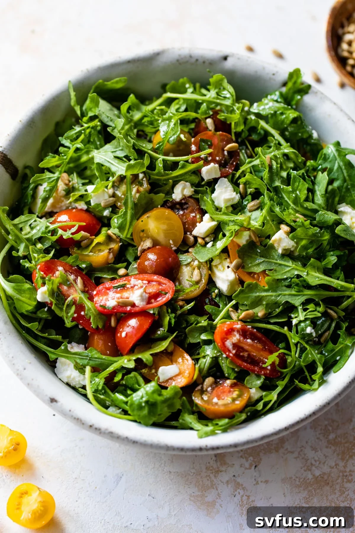 A close-up view of a vibrant arugula salad served in a bowl, generously garnished with bright red sliced grape tomatoes, emphasizing its fresh and appealing presentation.