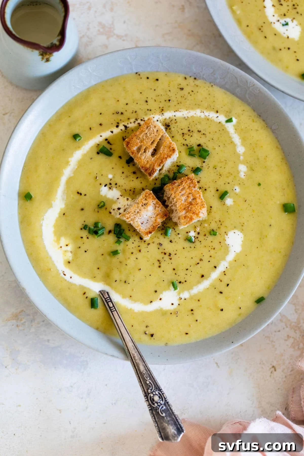 close-up of asparagus soup in a bowl with a spoon topped with a swirl of heavy cream and croutons