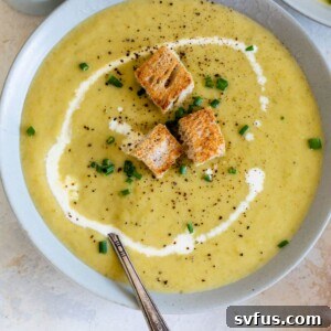 close-up of asparagus soup in a bowl with a spoon topped with a swirl of heavy cream and croutons