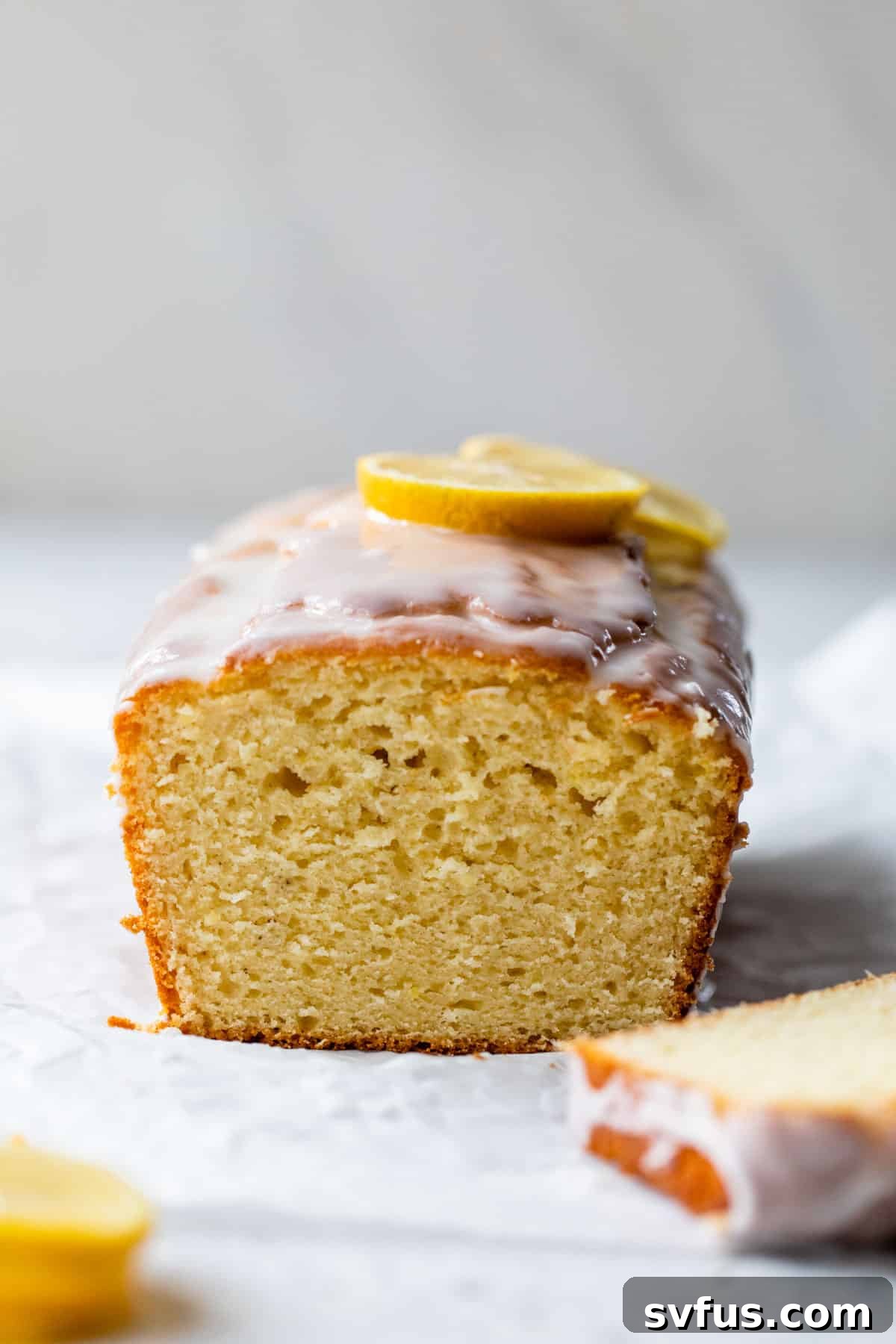 side view of lemon loaf with a slice cut off and lemon slices on top