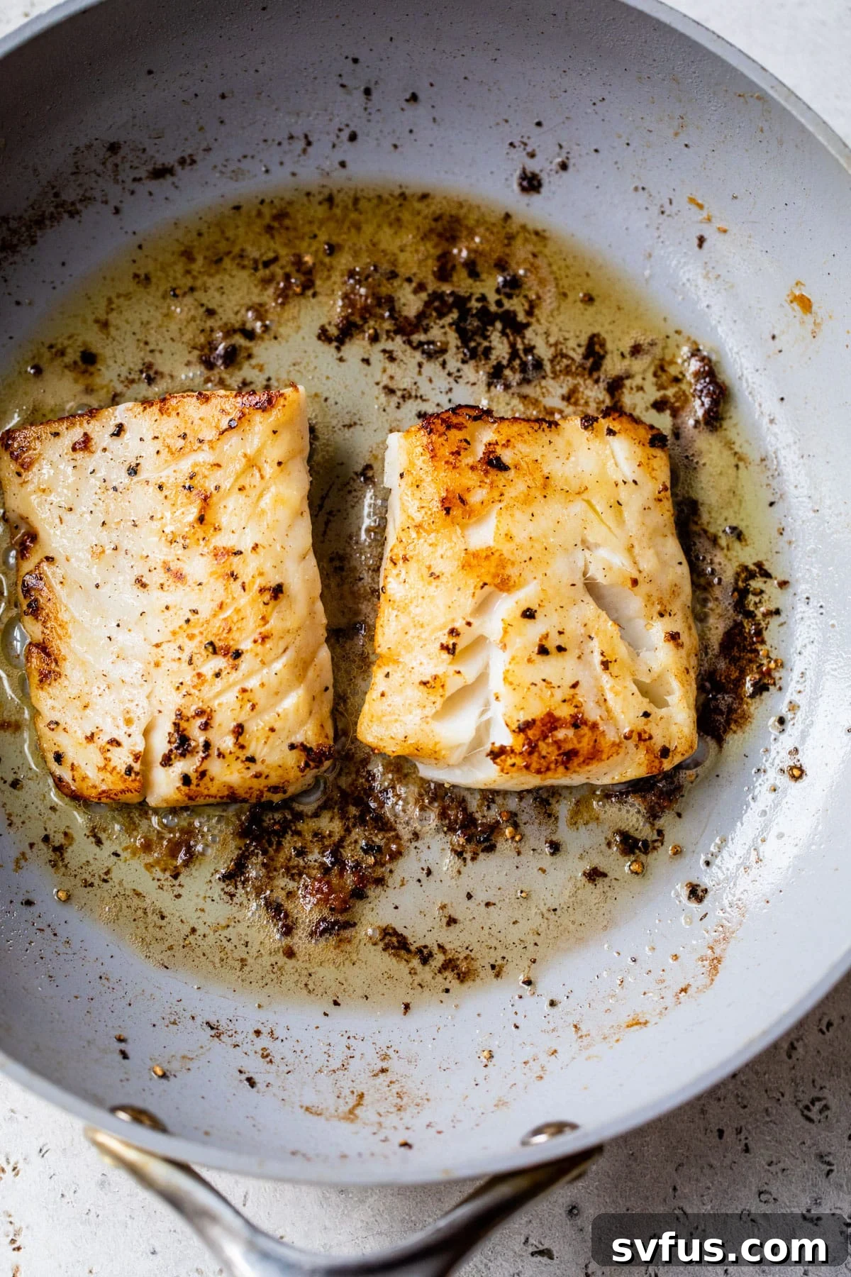 Two cod fillets sizzling in a hot nonstick skillet as they begin to develop a golden crust.