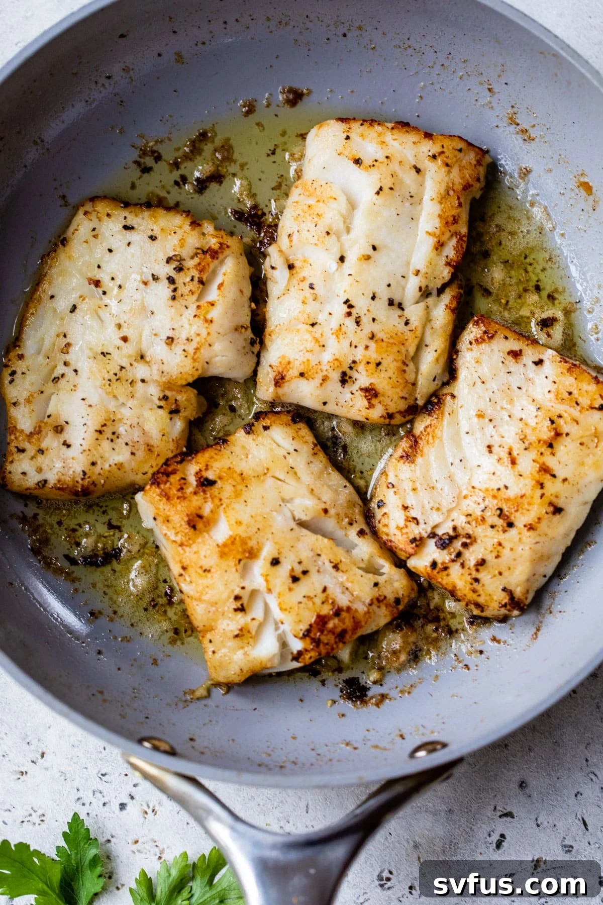 Four golden-brown cod fillets simmering in a rich garlic butter sauce in a skillet.