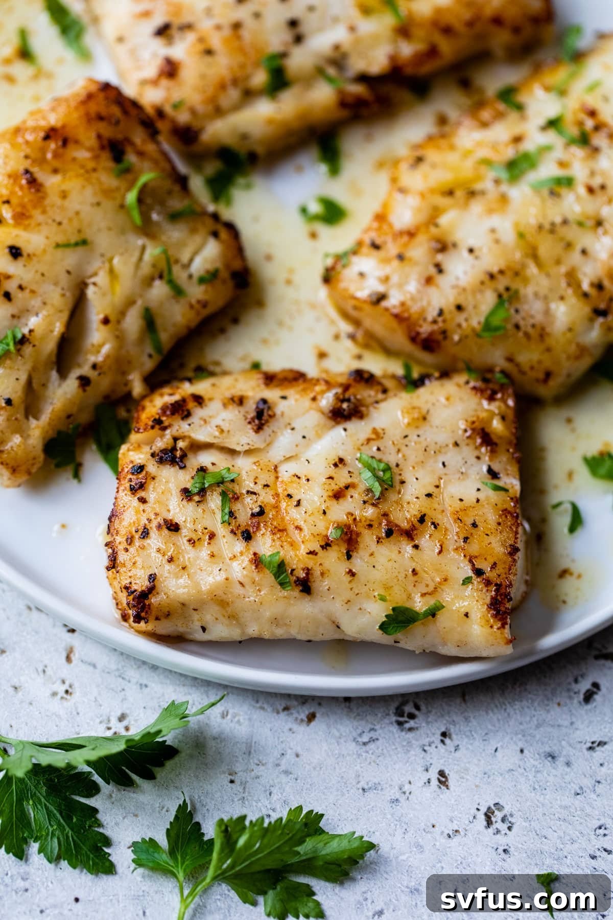 A beautifully plated pan-seared cod fillet, glistening with garlic butter sauce and topped with fresh parsley.