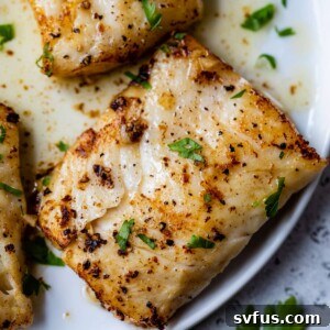 Close-up of pan-seared cod fillets on a plate with chopped parsley on top