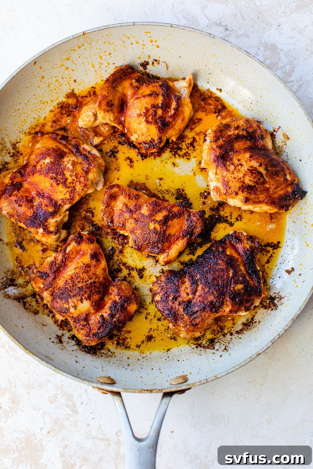 Two pieces of chicken thighs searing in a hot skillet with olive oil, developing a golden-brown crust.
