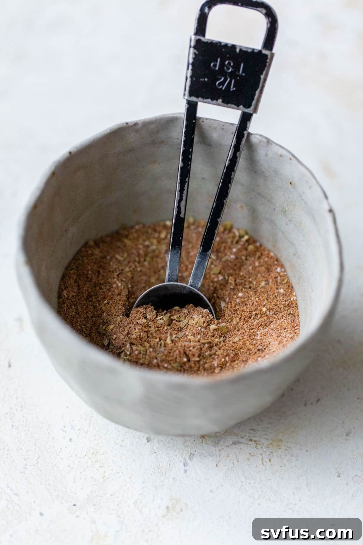 Fajita seasoning mixed together in a small bowl with a 1/2 tsp measuring spoon inside, ready to be used
