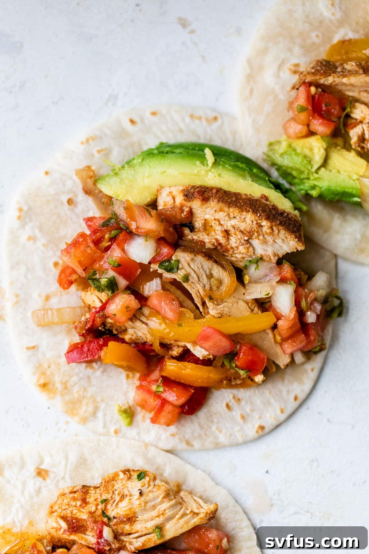 A perfectly assembled slow cooker chicken fajita on a tortilla, generously topped with fresh avocado slices and ready to eat