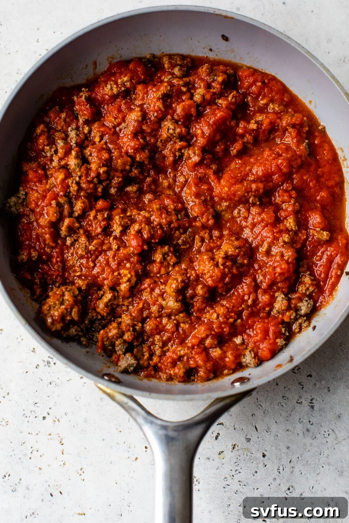 The vegan baked ziti meat sauce simmering in a large skillet, with plant-based beef coated in marinara.