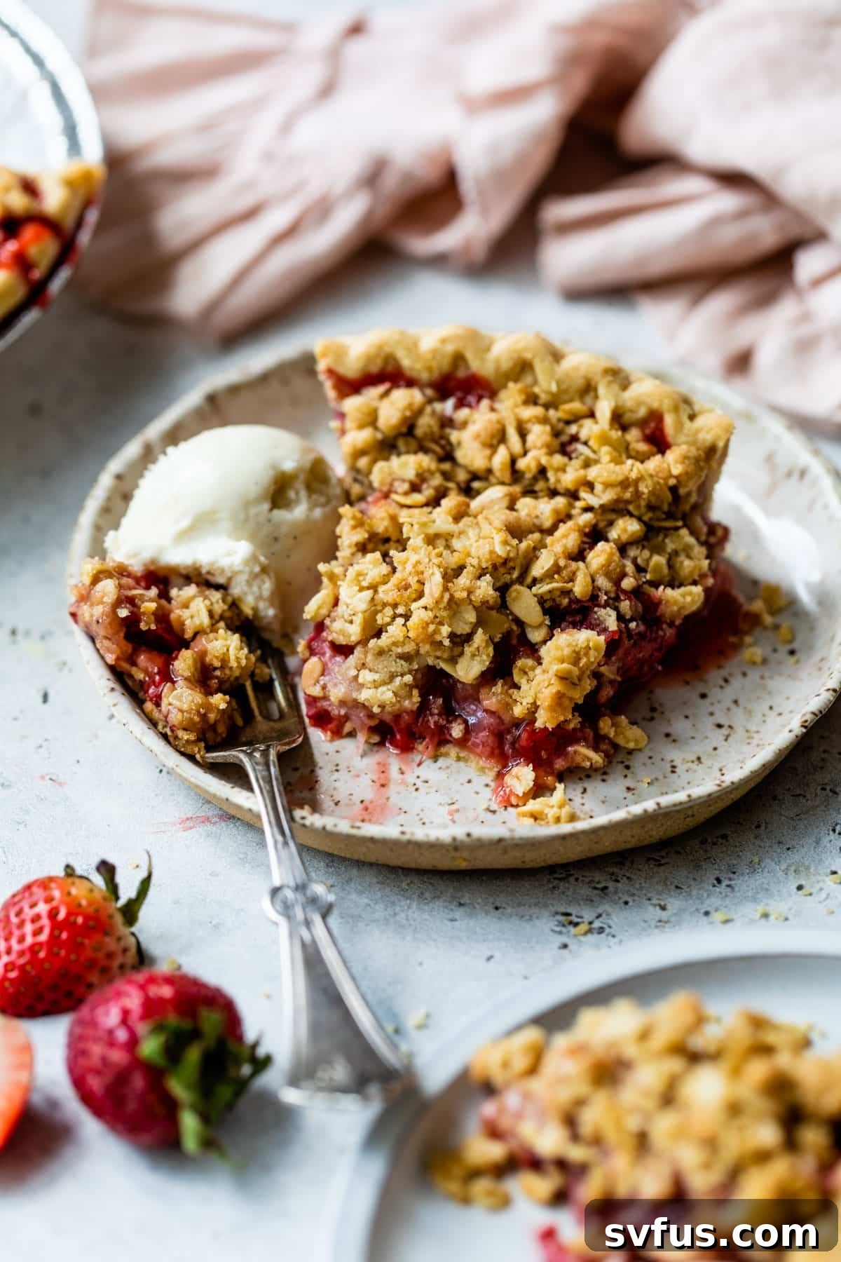 A vibrant slice of Strawberry Crumb Pie on a white plate, accompanied by a fork and a melting scoop of vanilla ice cream.