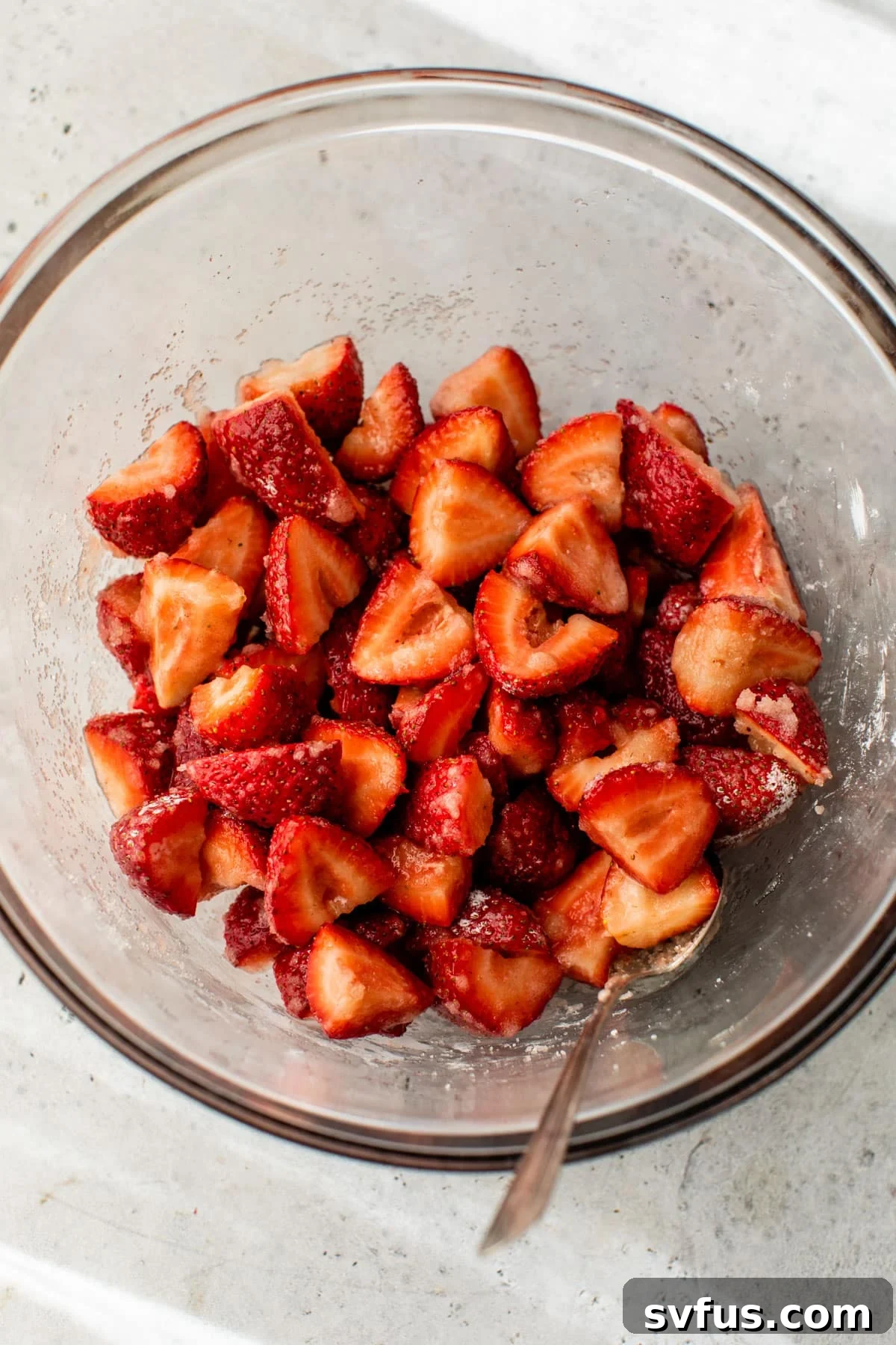 Fresh strawberries, granulated sugar, and cornstarch mixed in a glass bowl, ready for the pie filling.
