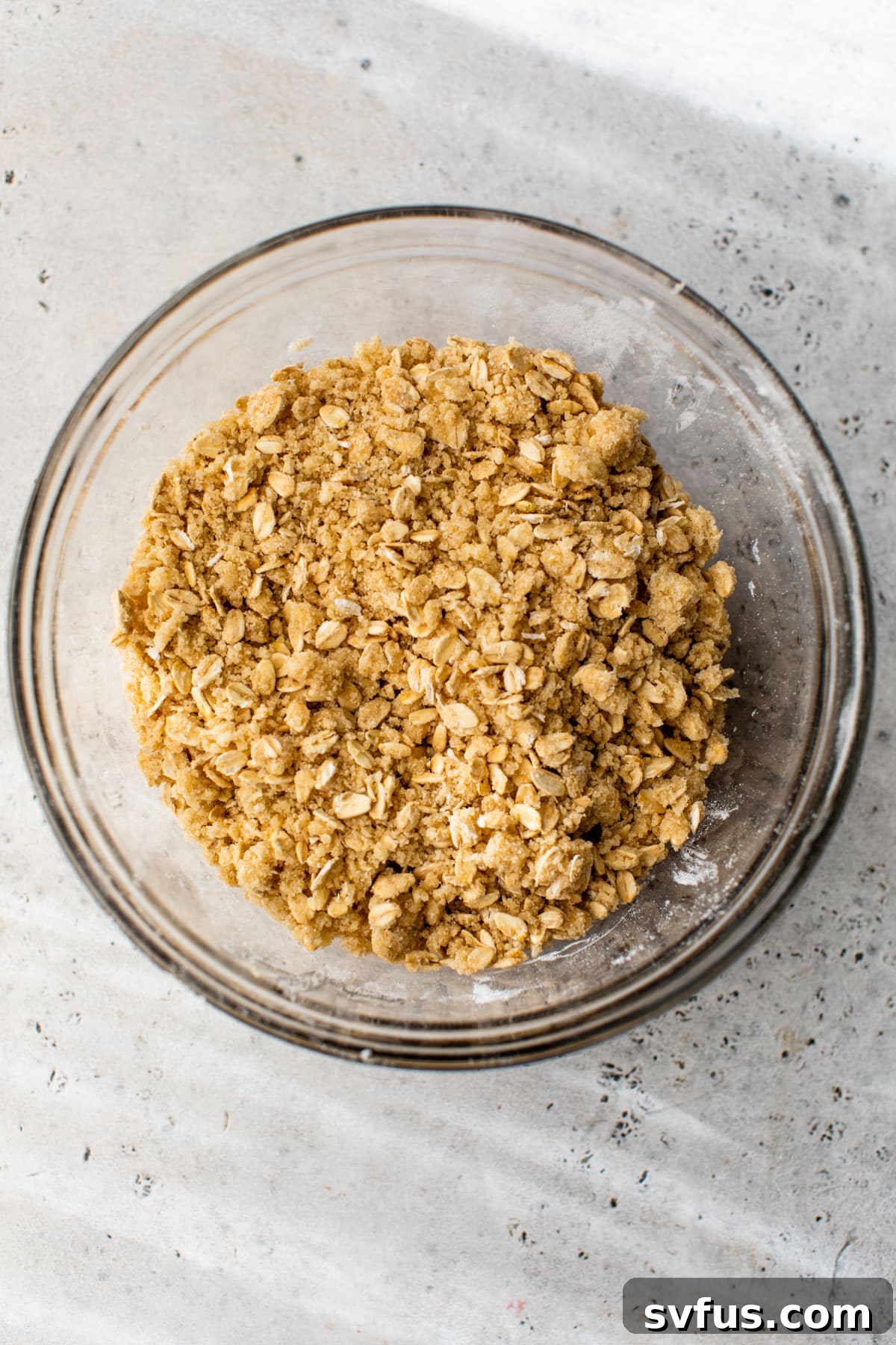 A glass bowl filled with the dry ingredients and cold butter chunks for the crumb topping, awaiting mixing.