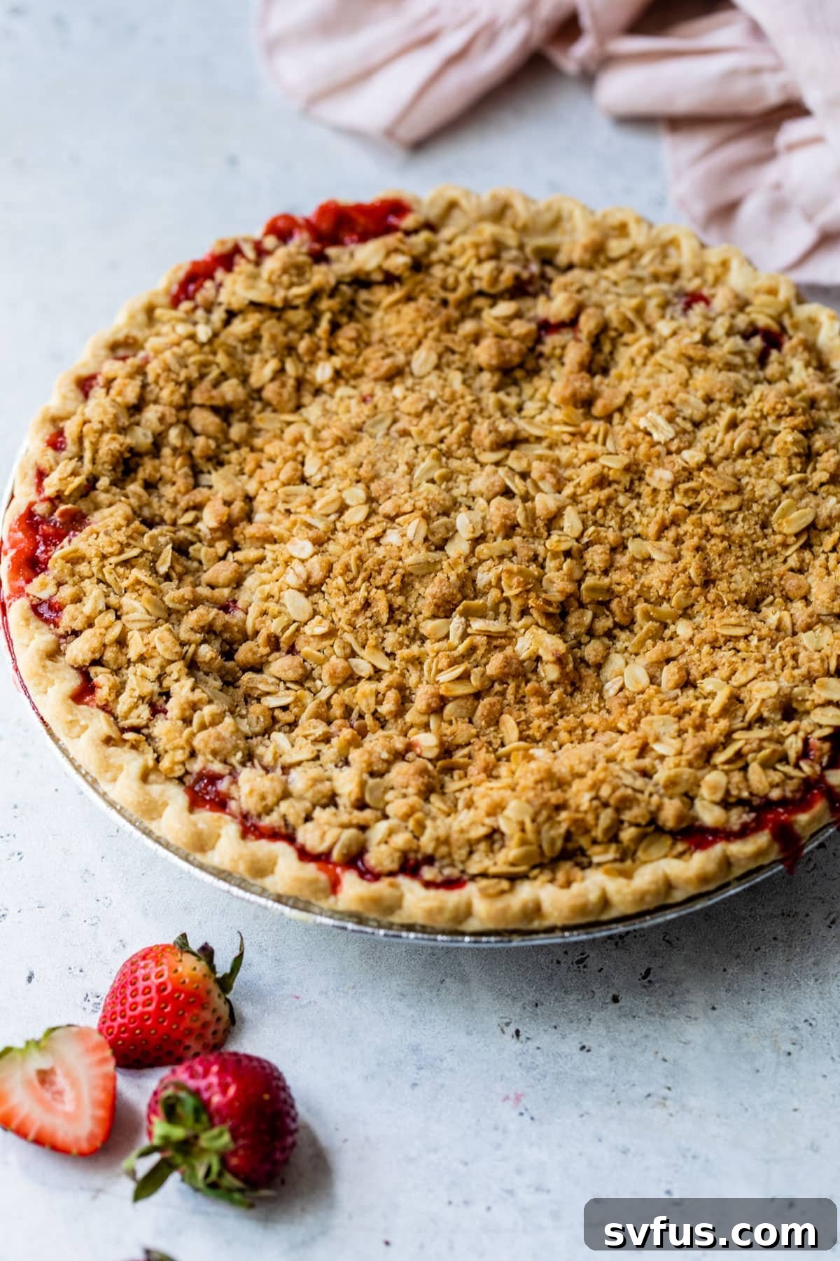 A freshly baked, whole Strawberry Crumb Pie with a golden-brown topping, resting on a table.