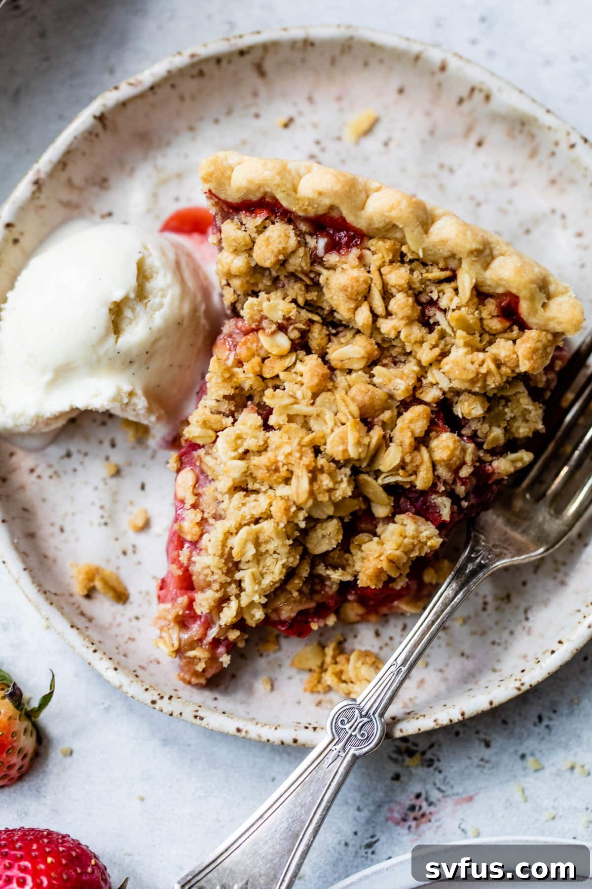 A close-up view of a slice of Strawberry Crumb Pie on a plate, showing the detailed crumb topping and fruit filling, with a fork and melting ice cream.