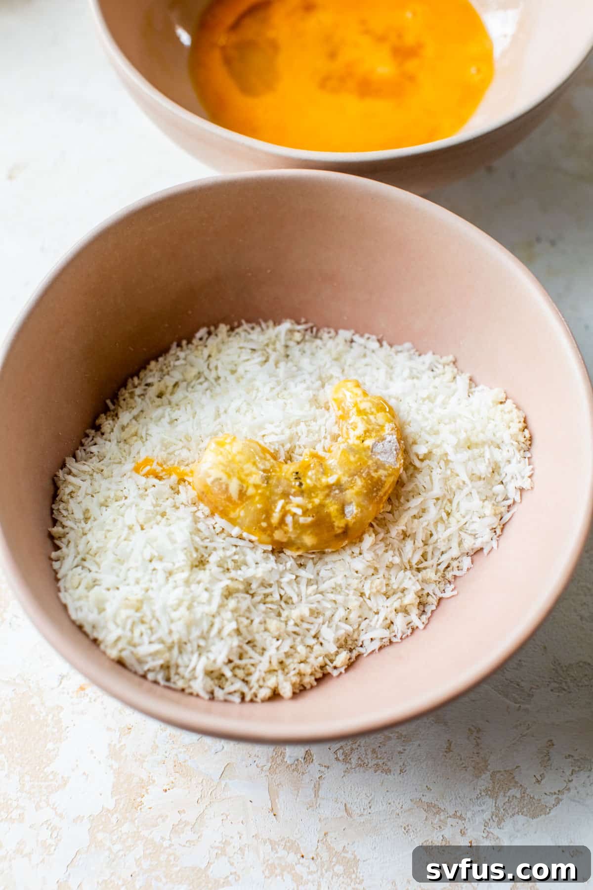 Shrimp being coated in a bowl of coconut flakes and panko after being dipped in egg wash