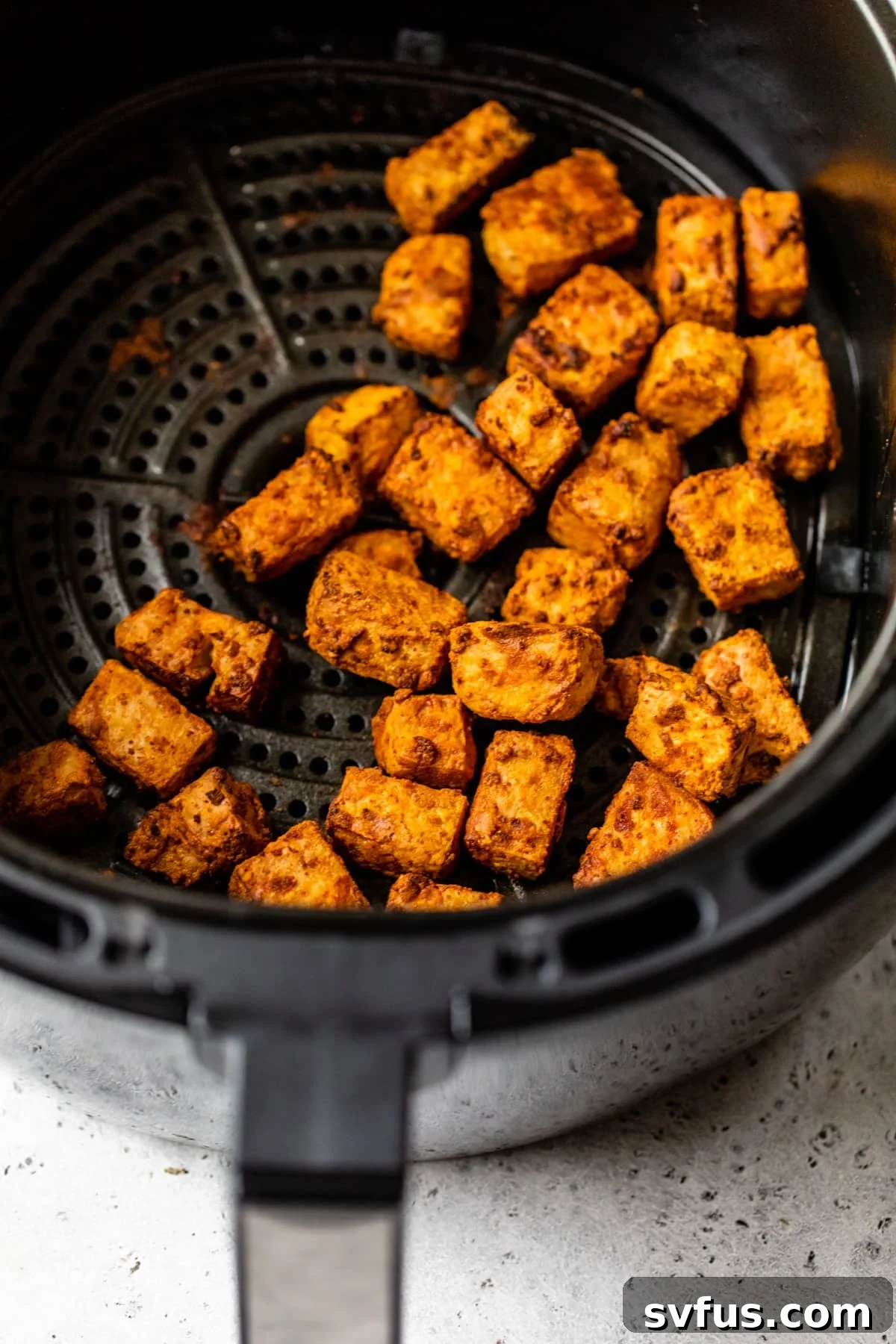 Close-up view of perfectly cooked, crispy air fryer tofu inside the air fryer basket.