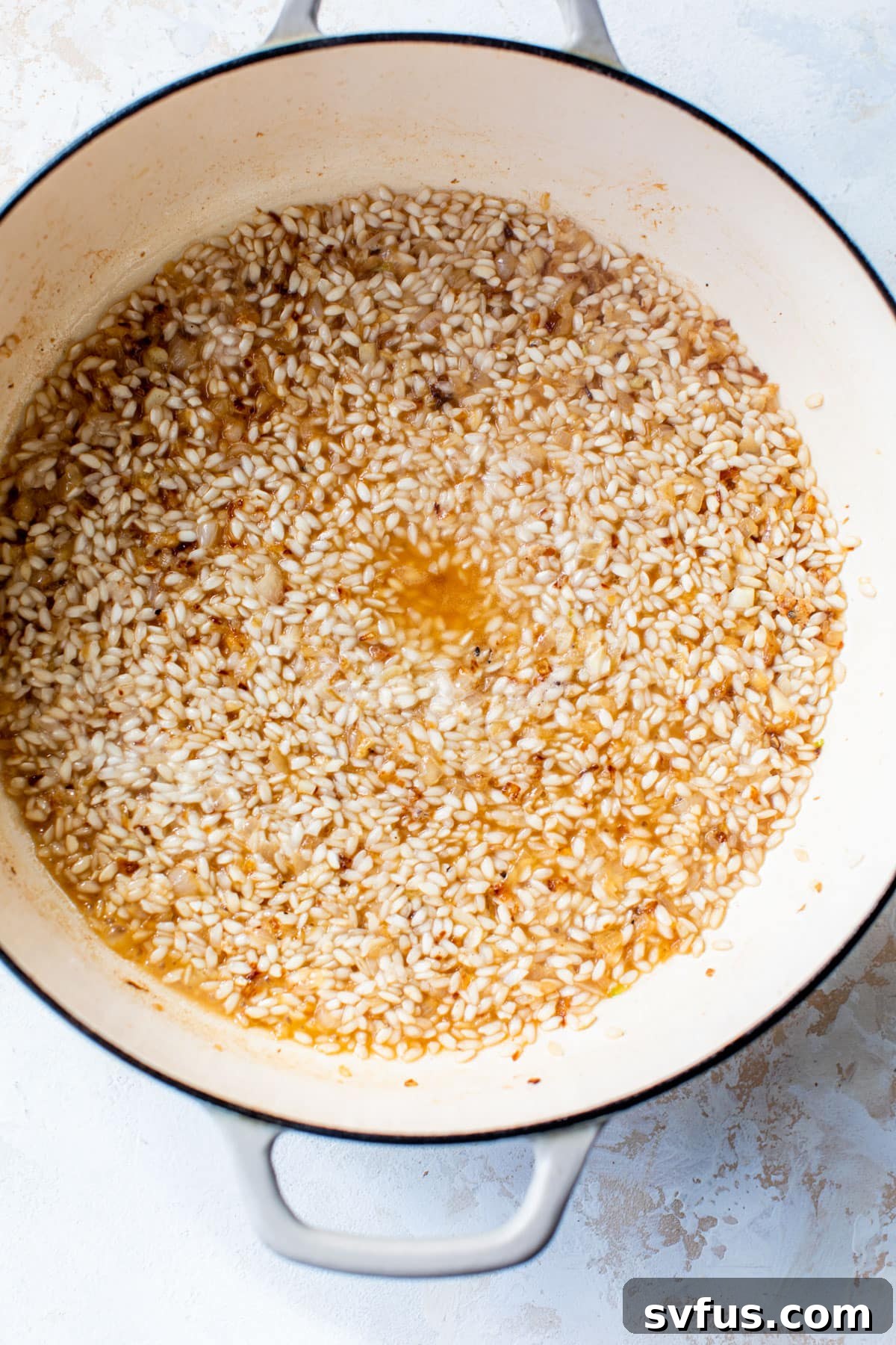 Dry white wine being poured into a Dutch oven with toasted Arborio rice, creating steam and a fragrant aroma.