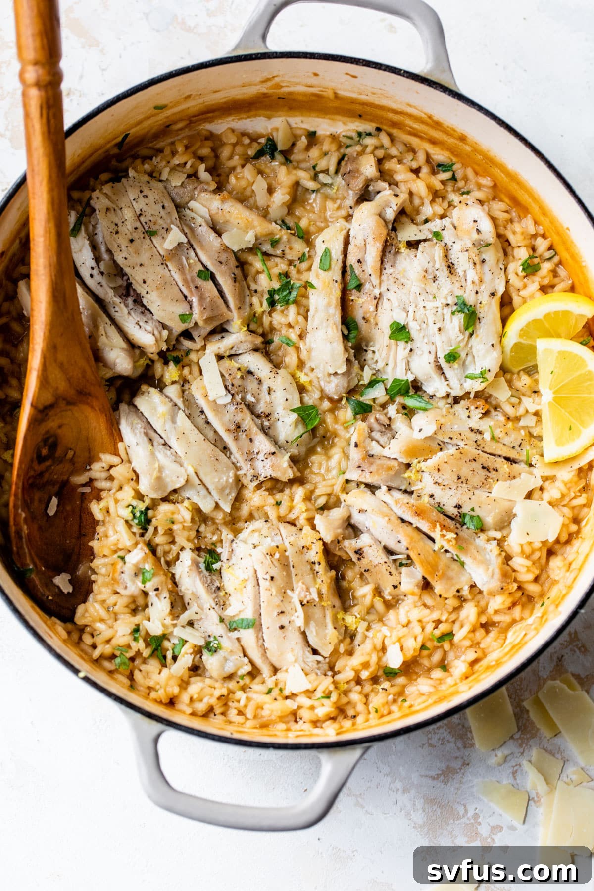 Perfectly cooked chicken added on top of creamy risotto in a Dutch oven, ready to be served with a wooden spoon.