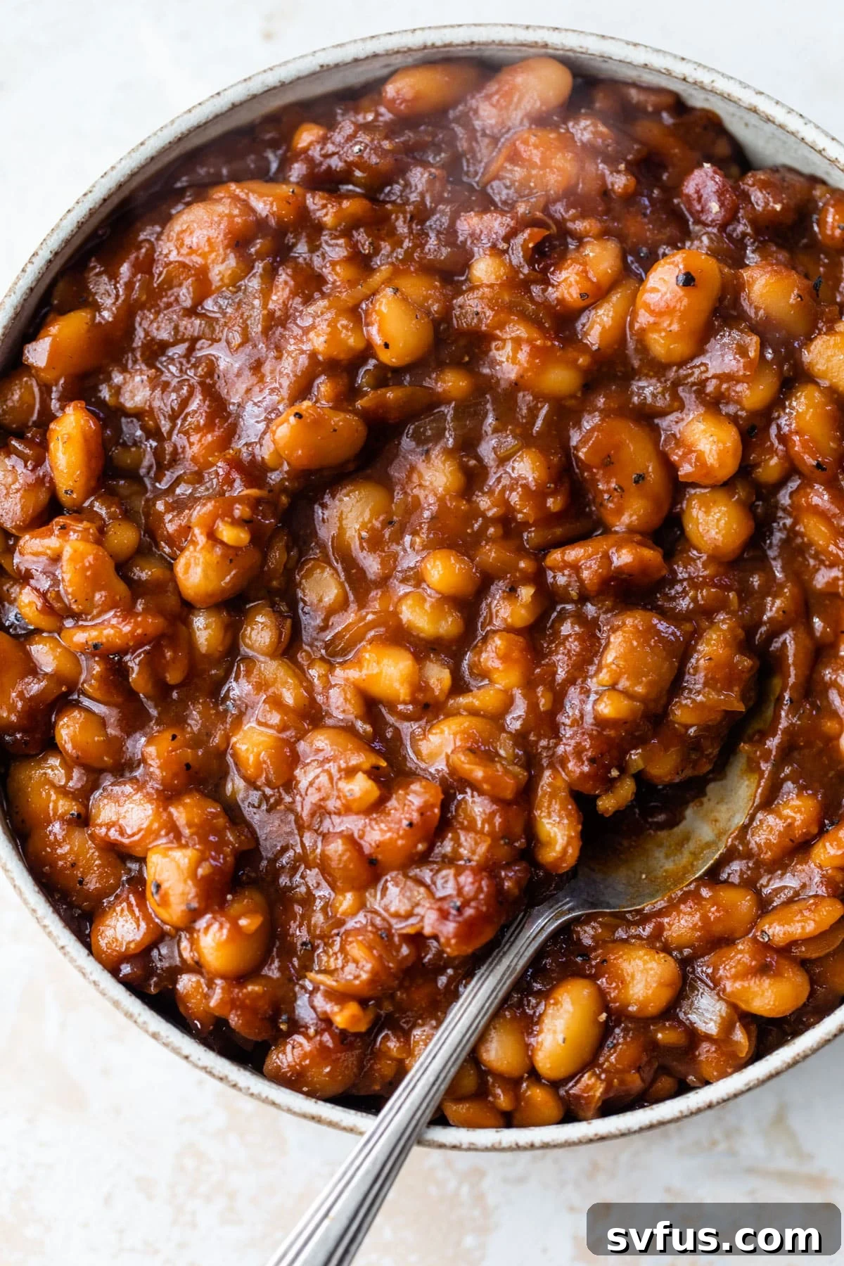 A close-up shot of a bowl of vegan baked beans with a spoon, highlighting the rich sauce and tender beans.