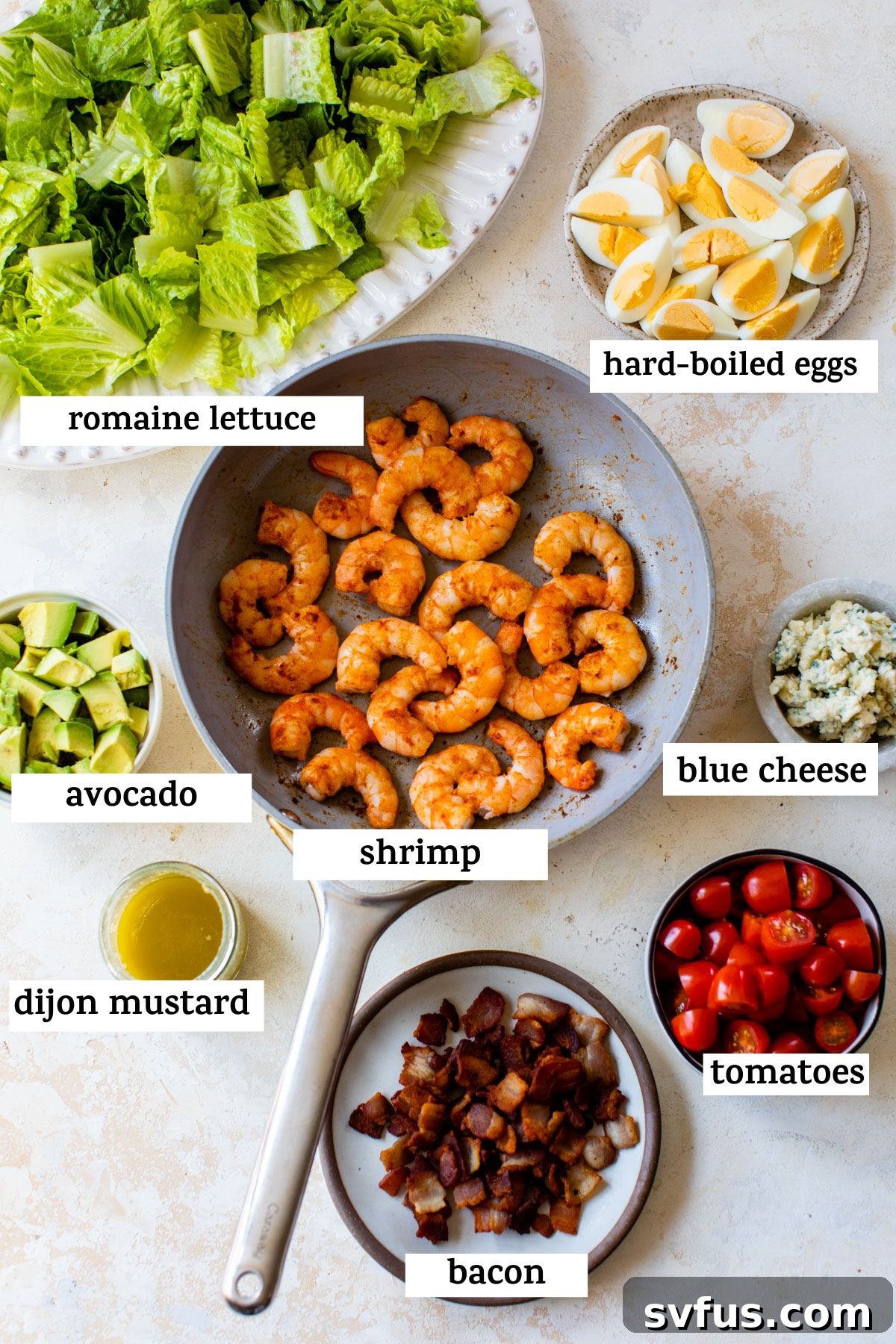 all ingredients on a table; romaine lettuce, hard-boiled eggs, avocado, shrimp, blue cheese, dijon mustard, bacon, and tomatoes